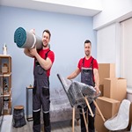 portrait-two-young-male-movers-loading-products-smiling-carrying-rolled-up-carpet-wrap-chair-210624843
